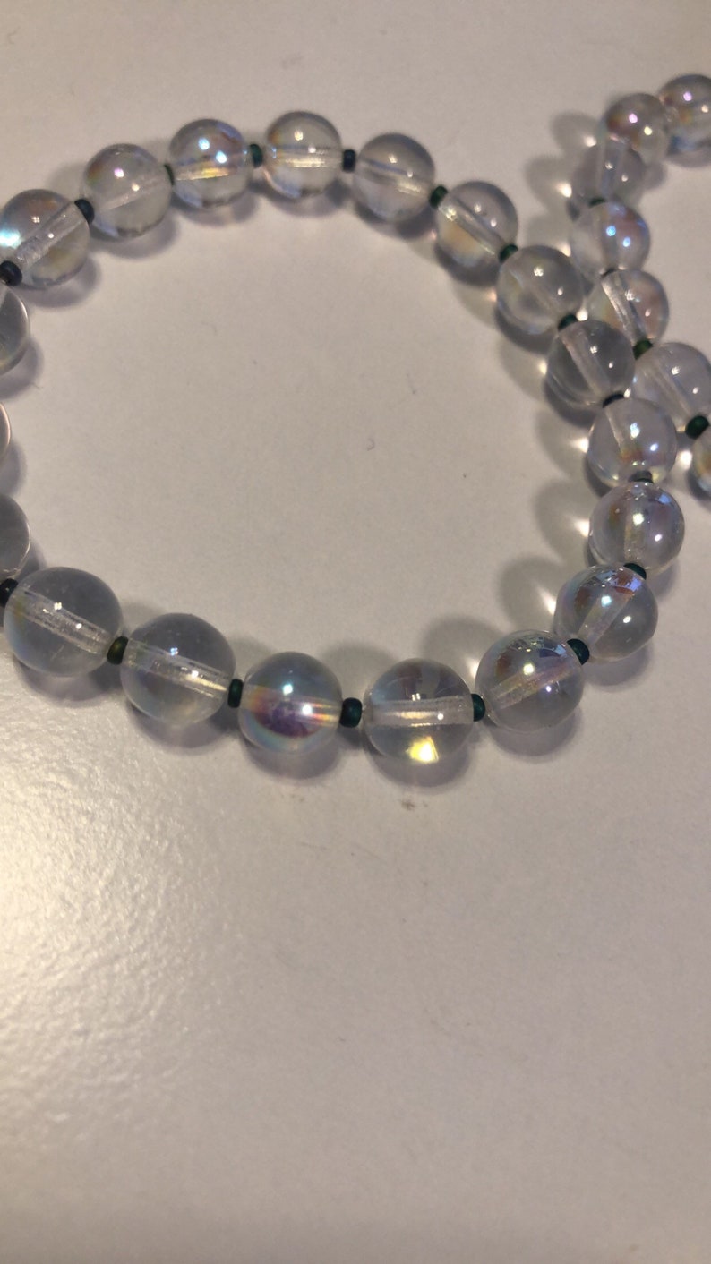 May include: A strand of iridescent clear glass beads with dark green spacers. The beads are round and have a slight shimmer.