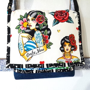 May include: A white messenger bag with a black strap and a flap featuring tattoo-style illustrations. The illustrations include a woman with flowers, a red rose, and the text "Only You". The bag has a blue denim base.