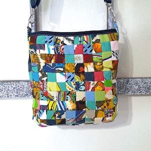 May include: A colorful patchwork crossbody bag with a woven design. The bag features a variety of fabric squares in shades of blue, green, red, yellow, and orange. It has a navy blue strap and trim, and silver-tone hardware.