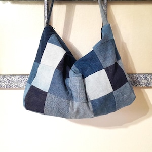 May include: A patchwork denim shoulder bag with a variety of blue hues. The bag is constructed from squares of different denim washes, creating a textured and visually interesting pattern. The bag has a single shoulder strap.