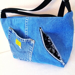 The back of a blue denim cross body bag with an opened zippered pocket.