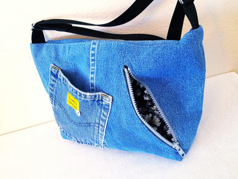 The back of a blue denim cross body bag with an opened zippered pocket.
