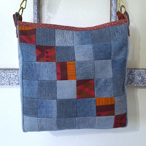 May include: A patchwork denim shoulder bag with a square shape. The bag features a grid pattern of various denim shades and colorful fabric squares in red and orange. The bag has a red trim and gold-colored chain straps.