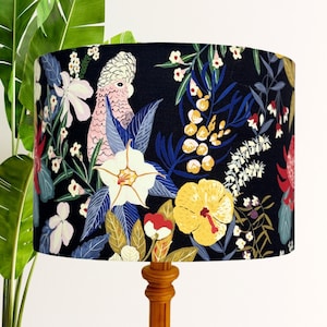 May include: A black lampshade with a floral print featuring pink cockatoos, white flowers, yellow flowers, and green leaves.