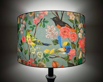 May include: A teal blue lampshade with a floral pattern featuring pink flowers, green leaves, and colourful birds. The birds are a yellow and green bird, a blue and black bird, and a black and orange bird.