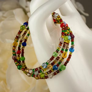 May include: A multi-strand wrap bracelet featuring a vibrant array of small glass beads in shades of red, green, yellow, blue, and clear. The bracelet is constructed with multiple circular loops, showcasing a mix of faceted and smooth round beads.