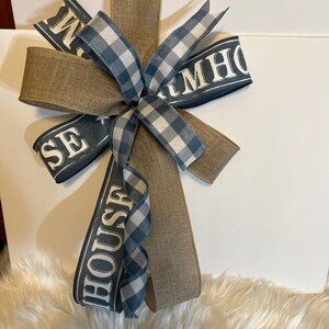 Könnte beinhalten: Eine Schleife im Landhausstil mit blau-weißem Gingham-Band, braunem Sackleinenband und blauem Band mit dem Text "FARMHOUSE" in Weiß.
