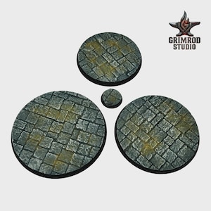 May include: A set of four circular bases with a cobblestone texture, in varying sizes. The bases are primarily gray with yellow highlights, suggesting an aged or weathered appearance. The Grimrod Studio logo is in the upper right corner.