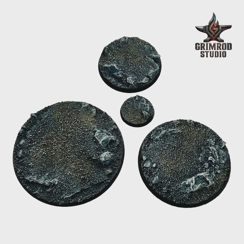 May include: Four textured, circular bases for miniature figures. The bases vary in size, with a rough, rocky surface in shades of gray and brown. The Grimrod Studio logo is in the upper right corner.