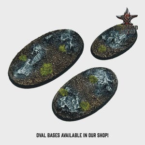 May include: Three oval-shaped miniature bases with textured surfaces, featuring a mix of dark gray, brown, and green elements. The bases have a rocky appearance with patches of green vegetation. Text at the bottom reads: OVAL BASES AVAILABLE IN OUR SHOP!