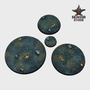 May include: Four textured, circular bases with a cracked, dark gray and brown surface. Small rocks and bone fragments are scattered across the bases. The Grimrod Studio logo is in the upper right corner.