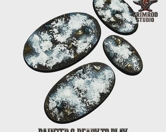 May include: Four oval-shaped miniature bases with a textured, snow-covered appearance. The bases are dark brown with white and gray accents, and the text "PAINTED & READY TO PLAY" is visible at the bottom. The Grimrod Studio logo is in the upper right corner.