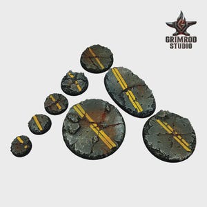 May include: A collection of miniature terrain bases, featuring a distressed asphalt design with yellow road markings. The bases vary in size and shape, with a cracked and weathered appearance. The Grimrod Studio logo is visible in the upper right corner.