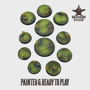May include: A collection of painted miniature bases, round and varying in size. The bases feature a green, grassy texture with small rocks, dried grass, and bone details. The text "PAINTED & READY TO PLAY" is displayed at the bottom.