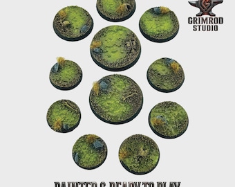 May include: A collection of painted miniature bases, round and varying in size. The bases feature a green, grassy texture with small rocks, dried grass, and bone details. The text "PAINTED & READY TO PLAY" is displayed at the bottom.