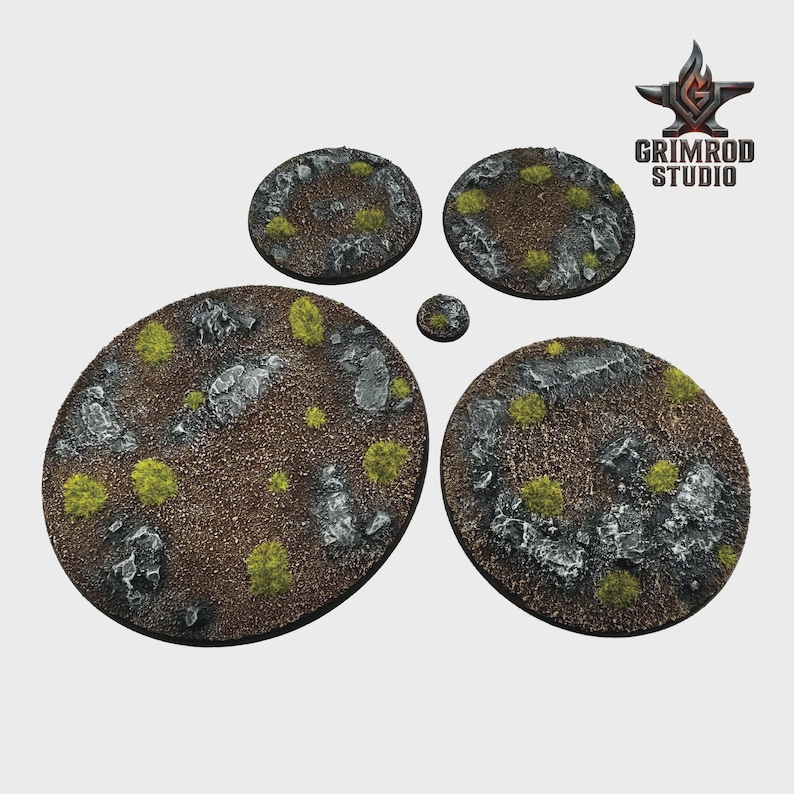 May include: A collection of textured, circular bases for miniature figures. The bases feature a brown, rocky terrain with patches of green vegetation and scattered gray stones. The Grimrod Studio logo is visible in the upper right corner.