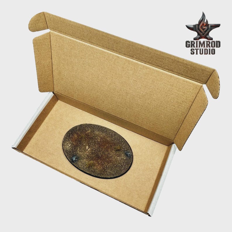 May include: An oval-shaped miniature base with a textured, earthy design, presented inside an open cardboard box. The base features a dark border and is likely for tabletop gaming miniatures. The Grimrod Studio logo is visible.
