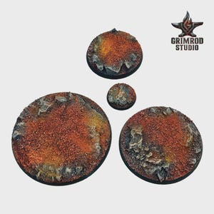 Pu&ograve; includere: Quattro basi circolari testurizzate per miniature. Le basi sono principalmente marrone-rossastro con macchie gialle e grigie, e presentano elementi rocciosi. Il logo Grimrod Studio &egrave; visibile in alto a destra.