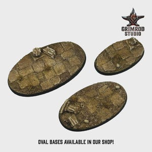 May include: Three oval-shaped bases with a textured, weathered appearance. The bases feature a cobblestone pattern with patches of grass and small stones. The bases are in varying sizes and are designed for miniature figures.