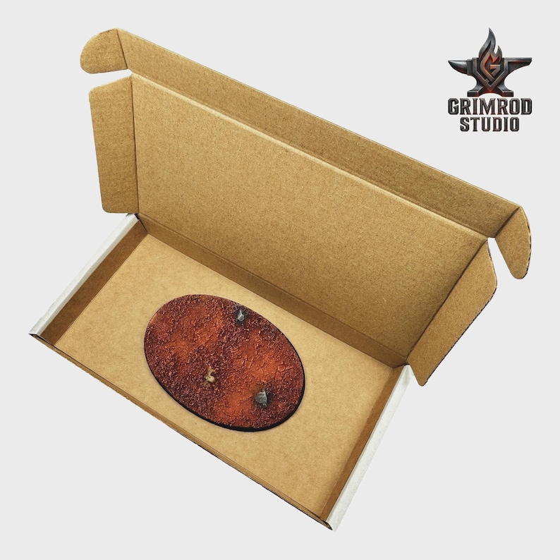 May include: An open cardboard box with a brown oval-shaped object inside. The object has a textured, reddish-brown surface with two small, silver-colored details. The box has the Grimrod Studio logo.