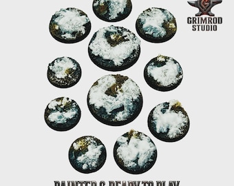 May include: A collection of eleven circular, miniature bases, painted with a snow-covered terrain effect. The bases vary in size and are arranged in a circular pattern. The text "PAINTED & READY TO PLAY" is at the bottom.