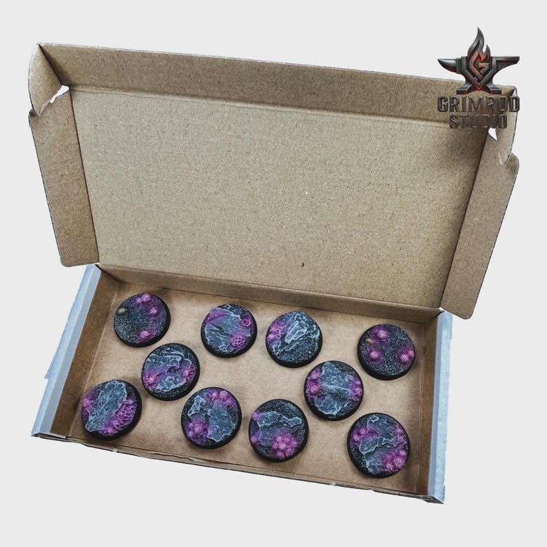 May include: A cardboard box containing ten round, miniature bases. The bases feature a textured, gray and black surface with purple and pink accents. The bases are for miniature gaming. The box has the Grimpod Studio logo.