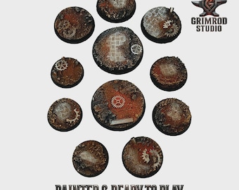 Può includere: Una collezione di undici basi circolari, strutturate con un'estetica steampunk. Le basi presentano tonalità marrone ruggine e arancione, con ingranaggi e dettagli di piastre metalliche incorporati. Il testo "PAINTED & READY TO PLAY" è in basso.