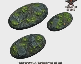 May include: Three oval-shaped miniature bases with a textured, painted terrain. The bases feature a mix of gray stone, green moss, and dark earth tones. The text "PAINTED & READY TO PLAY" is at the bottom, and the Grimrod Studio logo is in the upper right.