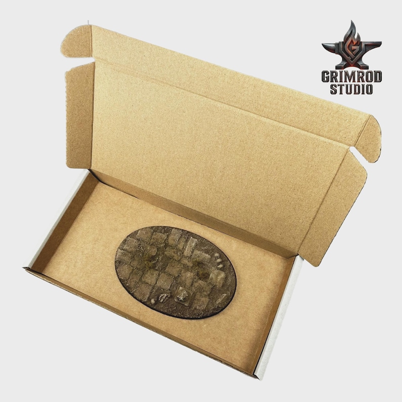 May include: An open cardboard box with a brown interior and a textured, oval-shaped base. The base has a cobblestone design. The Grimrod Studio logo is in the upper right corner.