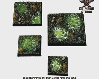 May include: Four square miniature bases with textured surfaces, featuring green and brown terrain with patches of grass and small rocks. The bases are painted and ready to play, as indicated by the text at the bottom of the image.