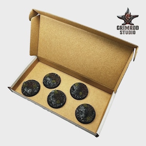 May include: A cardboard box containing five round, textured bases for miniature figures. The bases are dark brown with patches of green and gray, suggesting a terrain theme. The Grimrod Studio logo is visible in the upper right corner.