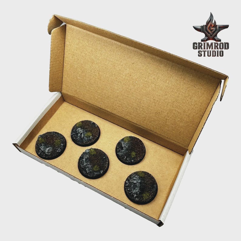 May include: A cardboard box containing five round, textured bases for miniature figures. The bases are dark brown with patches of green and gray, suggesting a terrain theme. The Grimrod Studio logo is visible in the upper right corner.