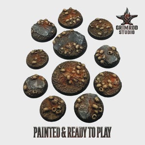 Può includere: Una collezione di undici basi rotonde in miniatura per giochi da tavolo. Le basi sono dipinte con un design terroso strutturato, con teschi e frammenti ossei. Il testo "PAINTED & READY TO PLAY" è visualizzato in basso.
