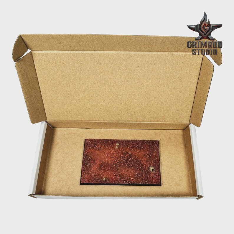 May include: An open cardboard box with a rectangular, reddish-brown item inside. The item has a textured surface with white speckles. The box has the text "GRIMROD STUDIO" and a logo on the top right corner.