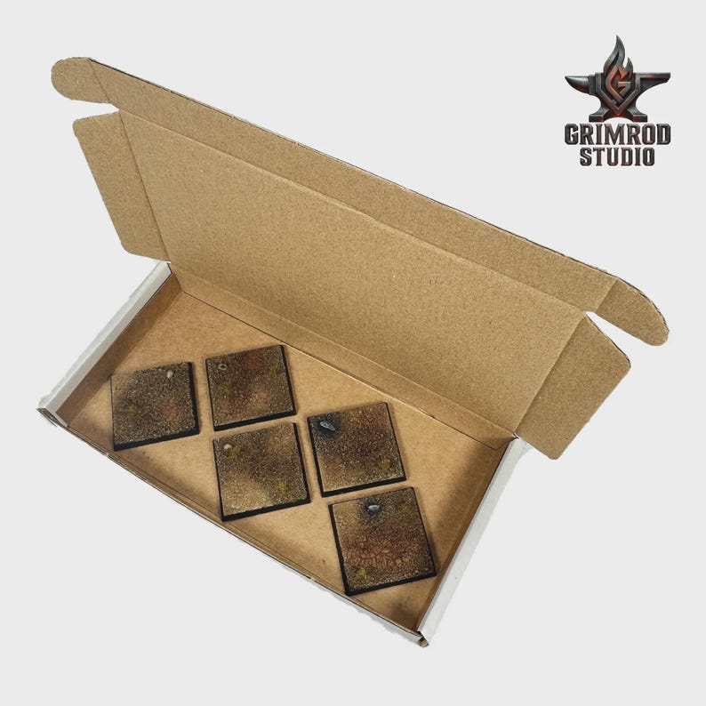 May include: A cardboard box with a white interior holds six square, textured bases. The bases have a brown and green mottled appearance. The Grimrod Studio logo is visible in the upper right corner.