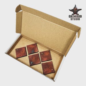 May include: A cardboard box with an open lid, revealing five square, textured, reddish-brown tiles. The tiles have dark edges and small details. The Grimrod Studio logo is in the upper right corner.