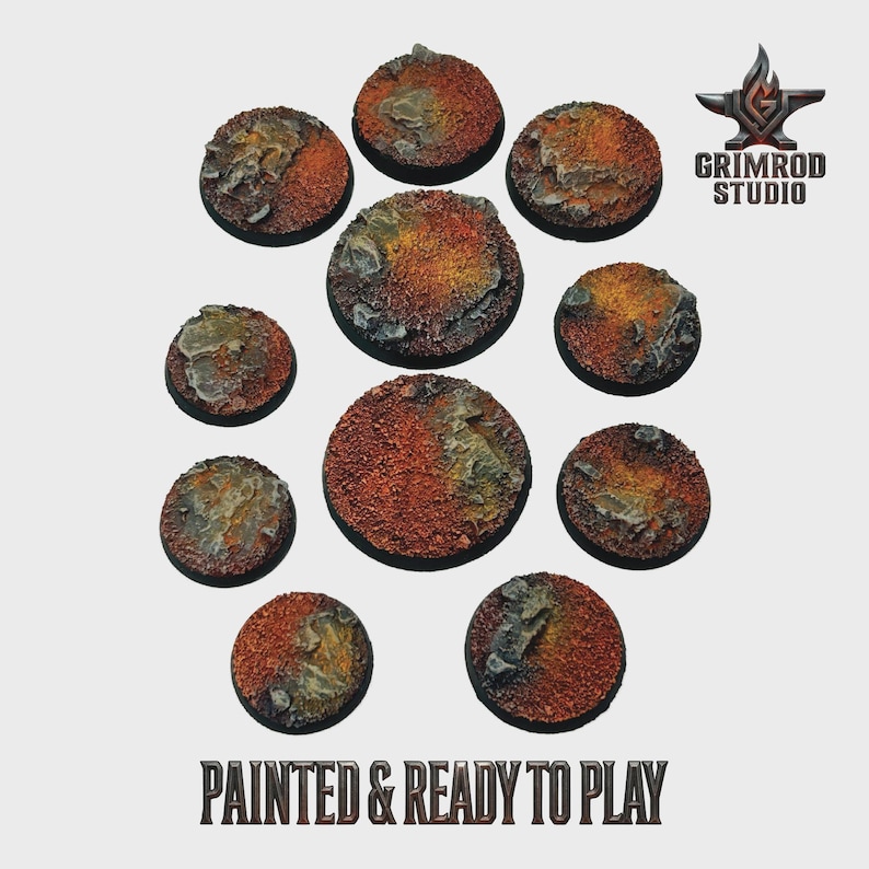 Pu&ograve; includere: Una collezione di dieci basi circolari e strutturate per miniature. Le basi sono dipinte con una combinazione di marrone rossiccio e giallo-arancio, con dettagli di roccia grigia. Il testo "PAINTED & READY TO PLAY" &egrave; visibile in basso.