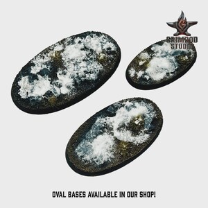 May include: Three oval bases with a textured, snow-covered terrain. The bases are dark brown with patches of green and white, and are designed for miniature figures. The text "OVAL BASES AVAILABLE IN OUR SHOP!" is at the bottom.