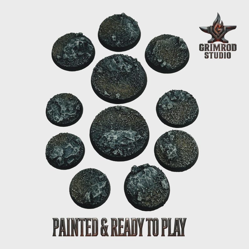 May include: A collection of eleven round, textured bases, painted in shades of gray and brown, arranged in a circular pattern. The bases have a rocky appearance with lighter gray accents. The text "PAINTED & READY TO PLAY" is at the bottom, with the Grimrod Studio logo in the upper right.