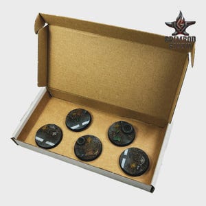 May include: A cardboard box with five circular, detailed bases for miniature figures. The bases feature a dark, textured surface with painted details, including road markings and foliage. The box has the Grimrod Studio logo.