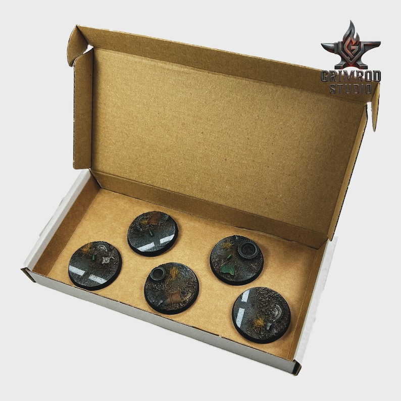 May include: A cardboard box with five circular, detailed bases for miniature figures. The bases feature a dark, textured surface with painted details, including road markings and foliage. The box has the Grimrod Studio logo.