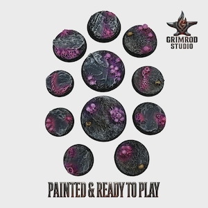 Könnte beinhalten: Eine Sammlung von zehn runden, strukturierten Basen, bemalt in Grau-, Schwarz- und Lilatönen. Die Basen weisen aufwendige Details auf und sind für Miniaturfiguren konzipiert. Der Text "PAINTED & READY TO PLAY" ist unten zu sehen.