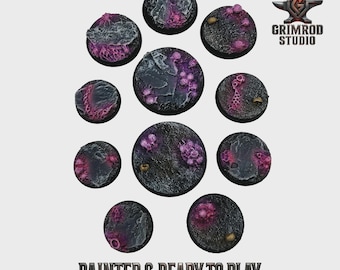May include: A collection of ten circular, textured bases, painted in shades of gray, black, and purple. The bases feature intricate details and are designed for miniature figures. The text "PAINTED & READY TO PLAY" is displayed at the bottom.