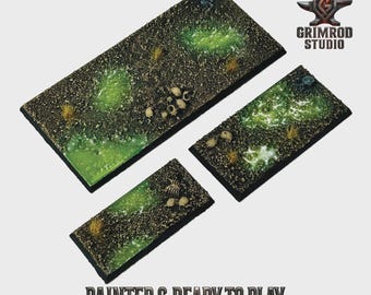 May include: Three rectangular terrain bases with a textured, dark brown surface, featuring patches of bright green, resembling a swamp. Small skulls and bones are scattered across the surface. The text "PAINTED & READY TO PLAY" is visible.