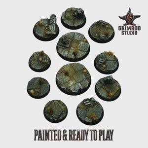 Può includere: Una collezione di dieci basi circolari in miniatura, dipinte per assomigliare a pietra erosa con erba e detriti. Le basi sono disposte a cerchio. Il testo "PAINTED & READY TO PLAY" è in basso. Ideale per giochi da tavolo.