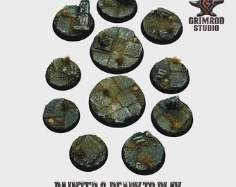 May include: A collection of ten circular, miniature bases, painted to resemble a weathered stone surface with patches of grass and debris. The bases are arranged in a circular pattern. The text "PAINTED & READY TO PLAY" is at the bottom.