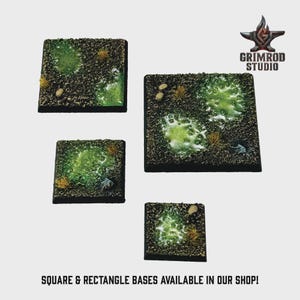 May include: Four square and rectangular miniature bases with a textured, dark brown surface. Each base features patches of green, light green, and yellow-brown vegetation, with small rocks. The text "SQUARE & RECTANGLE BASES AVAILABLE IN OUR SHOP!" is at the bottom.