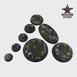 May include: A collection of textured, circular and oval miniature bases. The bases are dark gray with patches of green and white, resembling a rocky terrain. The Grimrod Studio logo is in the upper right corner.