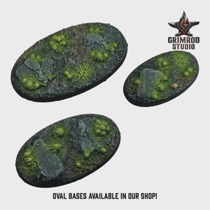 May include: Three oval-shaped miniature bases with textured surfaces. The bases feature a mix of gray, green, and brown tones, with simulated rock and vegetation. The text "OVAL BASES AVAILABLE IN OUR SHOP!" is at the bottom. The Grimrod Studio logo is in the top right.