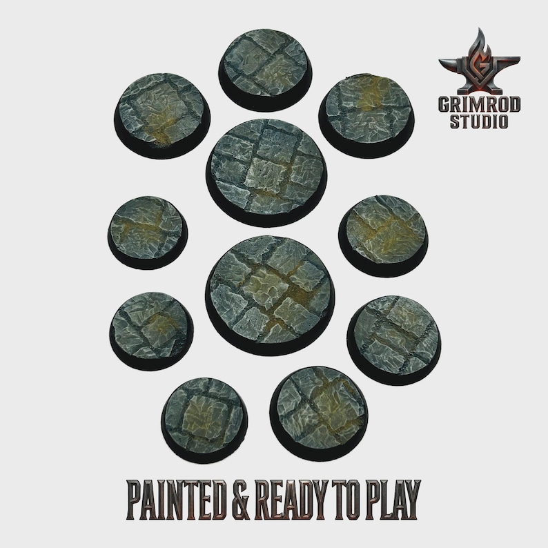 May include: A collection of eleven circular, stone-textured bases, painted in shades of gray and brown, arranged on a light background. The bases vary in size and feature a cobblestone pattern. The text "PAINTED & READY TO PLAY" is at the bottom.